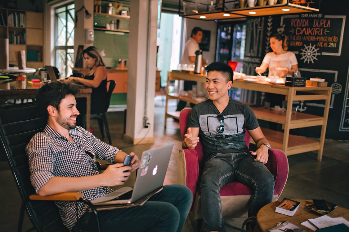 Two guys sitting in comfy cafe chairs, smiling
