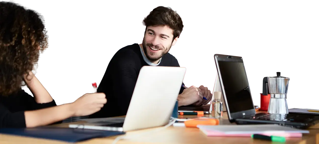 Two colleagues talking across a shared desk with their laptops open