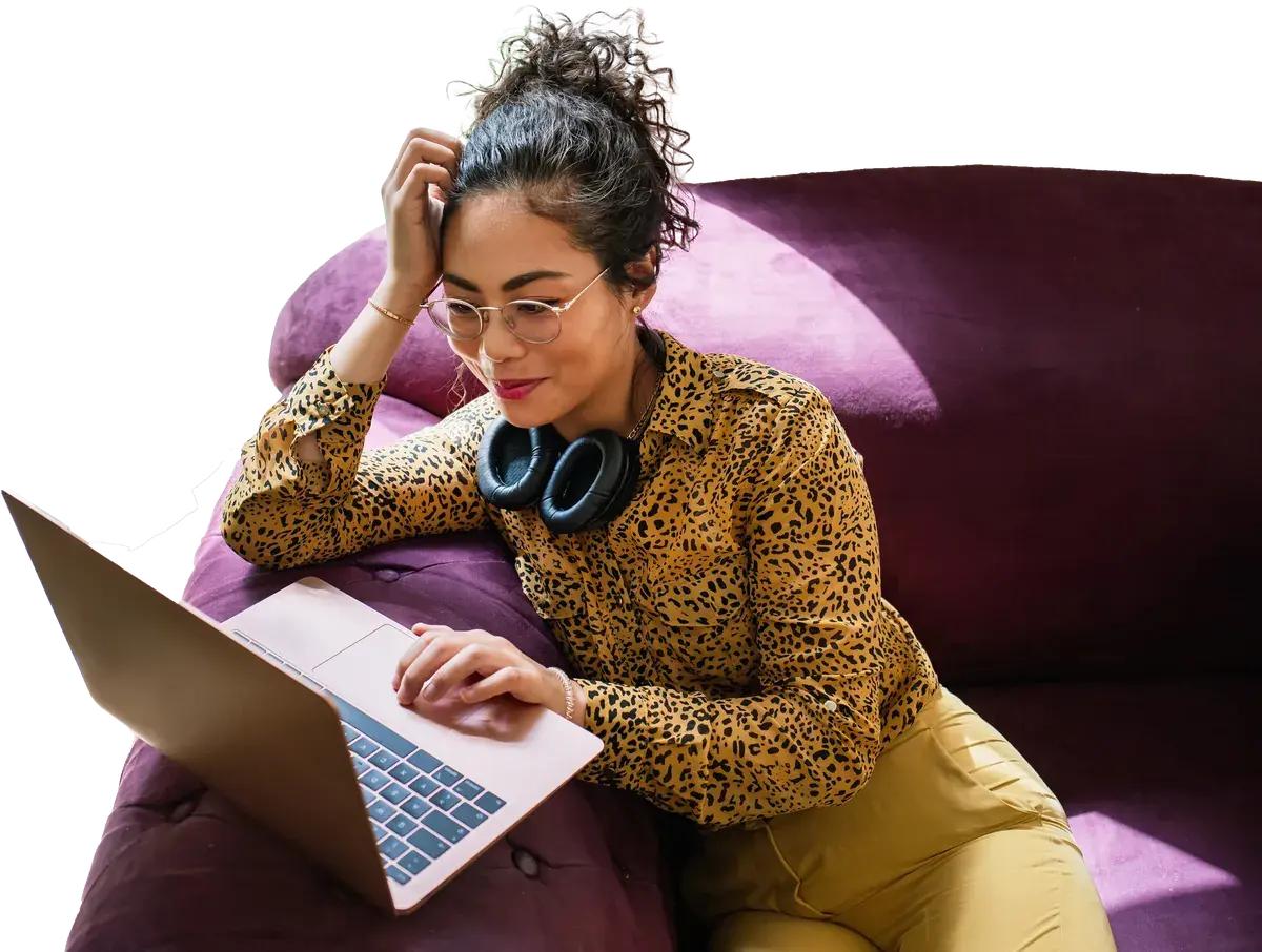 A woman in headphones works on a laptop from a sofa